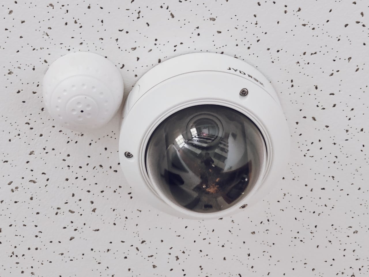about-me-02 Close-up of a round dome surveillance camera installed on a speckled ceiling for security monitoring.